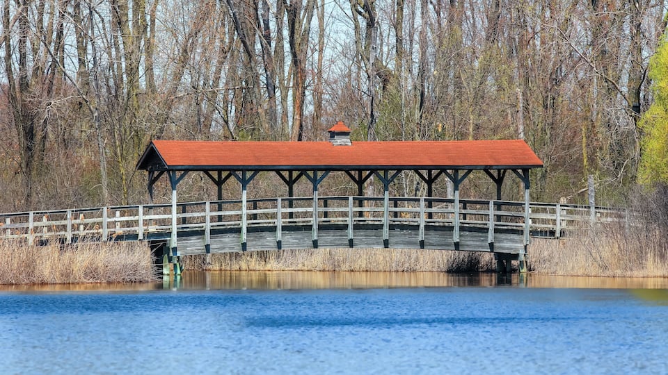 A wooden bridge with a red roof over a body of water, surrounded by trees.