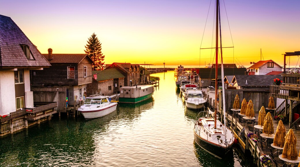 A marina with boats docked, wooden buildings, and a sunset in the background.