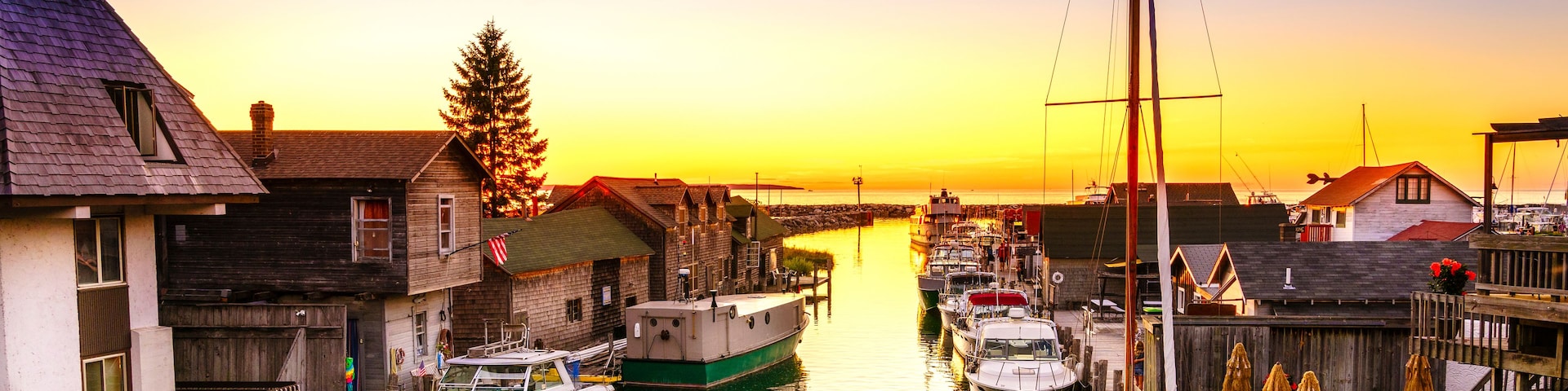 Un puerto deportivo con barcos amarrados, edificios de madera y un atardecer al fondo.