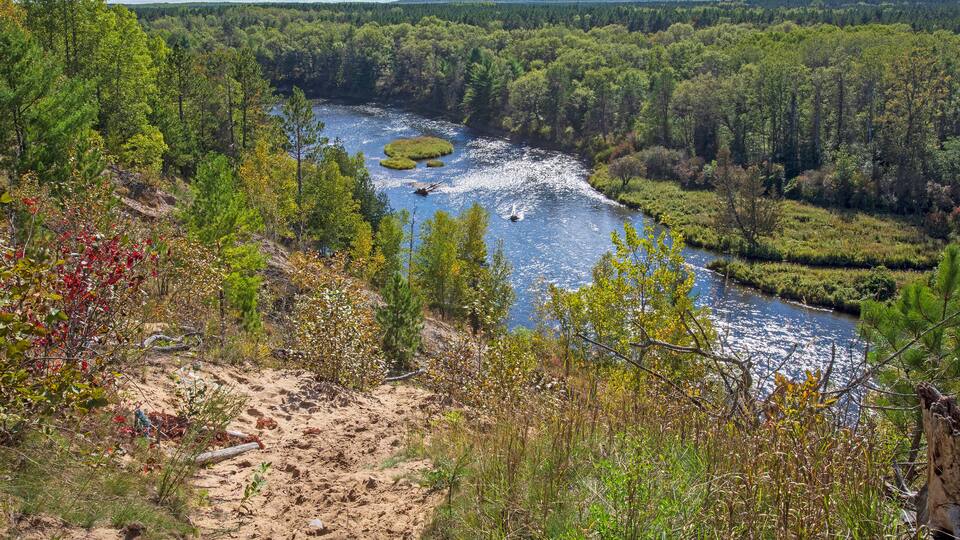 A river winding through a forested valley with a sandy path leading to a viewpoint overlooking the water.