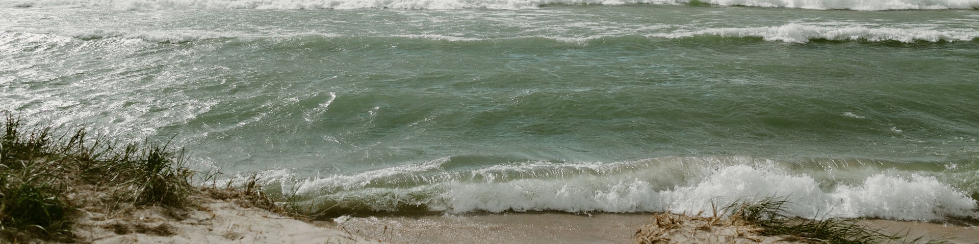 A beach with waves crashing onto the shore under a partly cloudy sky.
