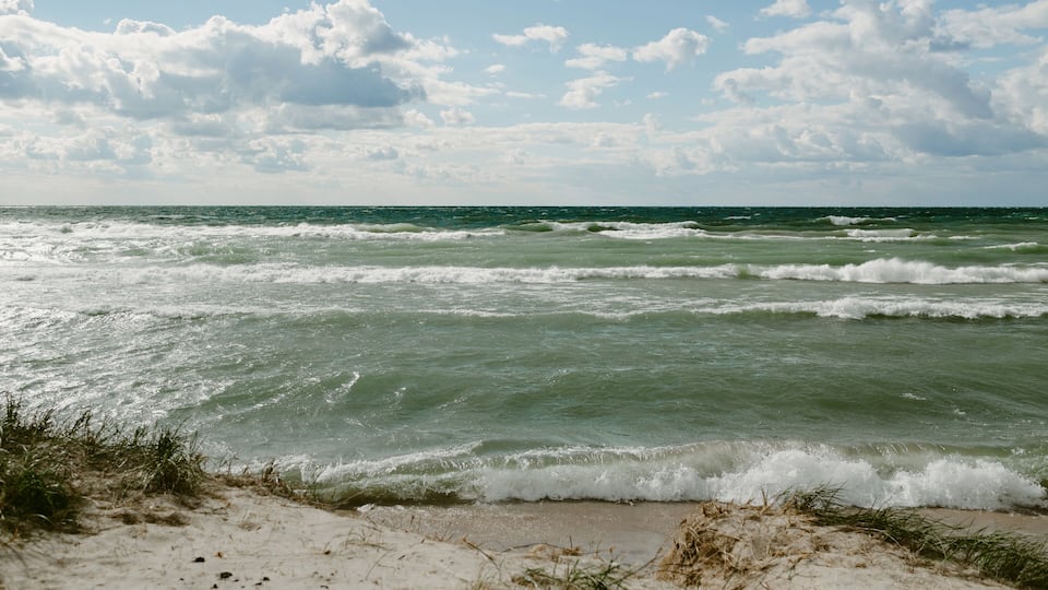 A beach with waves crashing onto the shore under a partly cloudy sky.