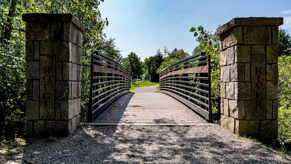 A stone bridge with metal railings, surrounded by trees and greenery.