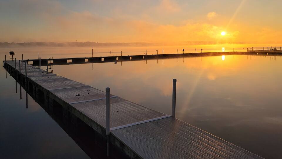 A wooden pier extending into calm water at sunrise with the sun low on the horizon.