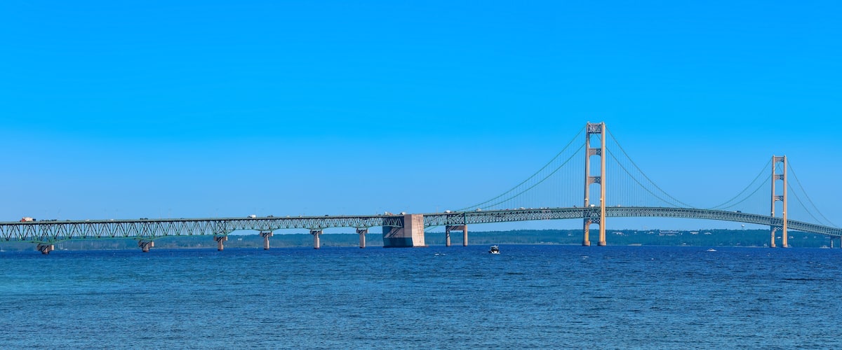A large suspension bridge spanning a wide river with multiple lanes of traffic and a boat in the water.