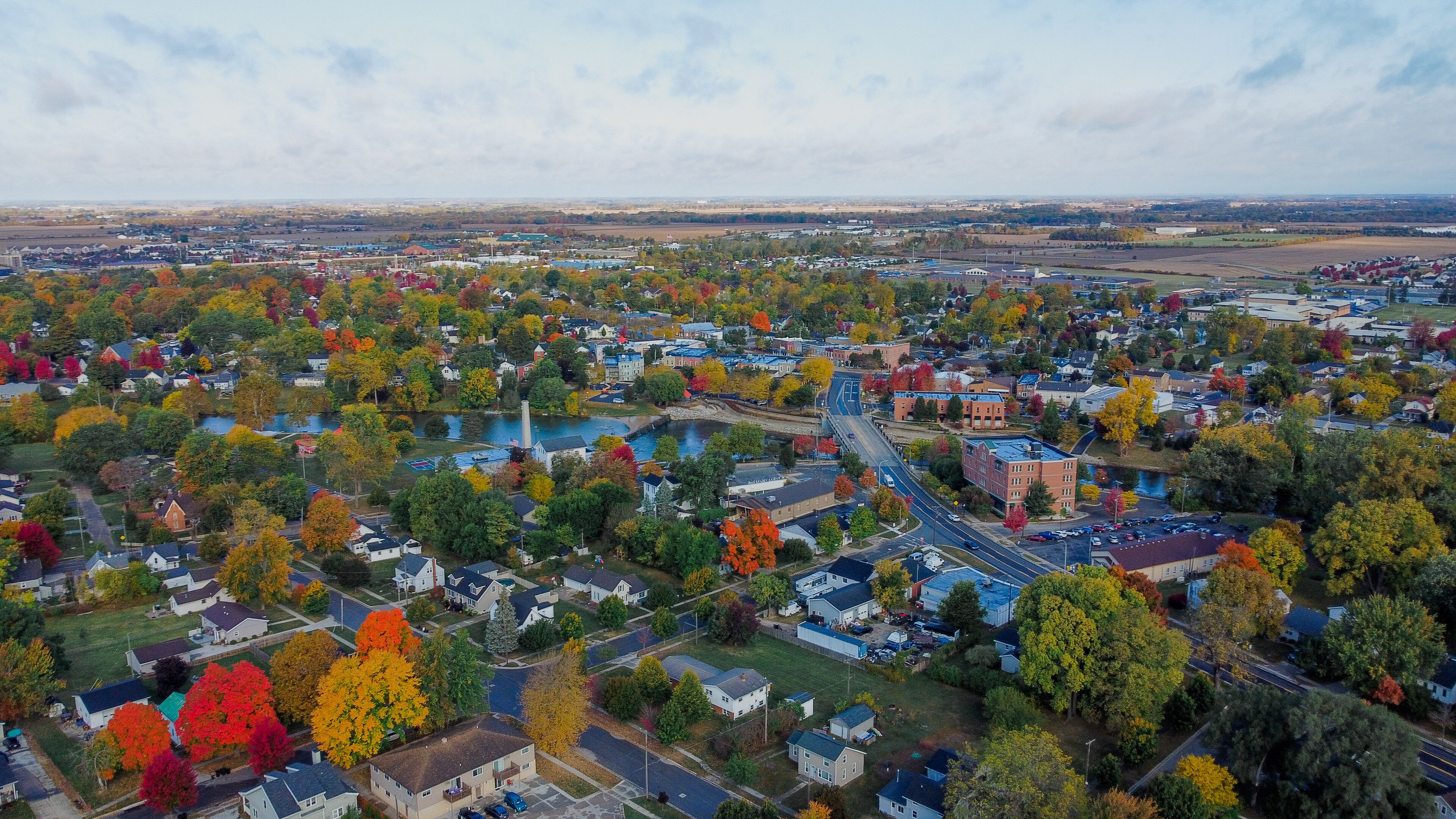 An aerial view of a town with autumn foliage, a river, and a bridge.