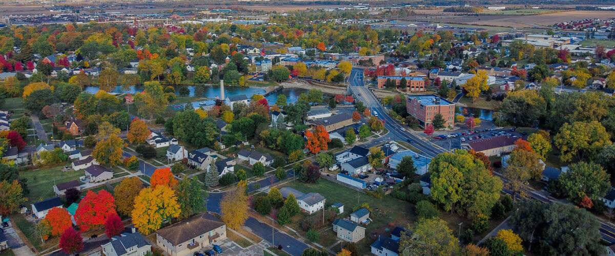 An aerial view of a town with autumn foliage, a river, and a bridge.