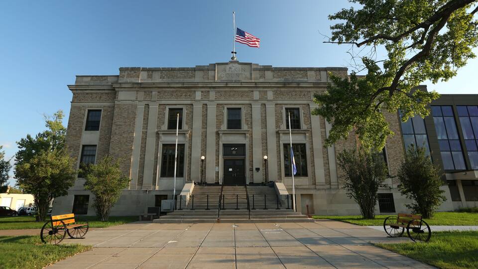 A historic courthouse with a flagpole, steps, and benches.