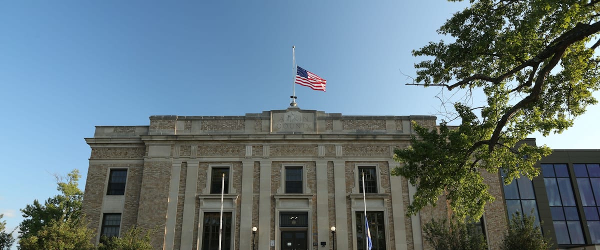 A historic courthouse with a flagpole, steps, and benches.