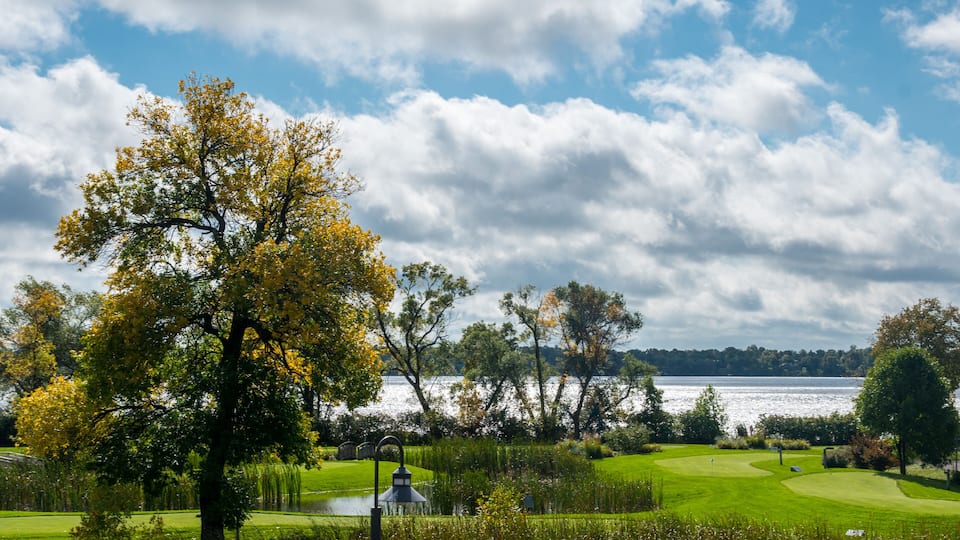 A golf course with a lake, trees, and a cloudy sky.