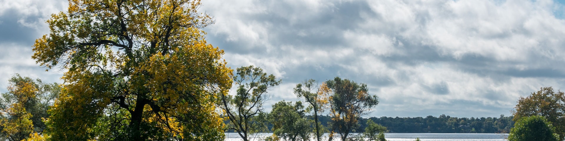 Um campo de golfe com um lago, árvores e um céu nublado.