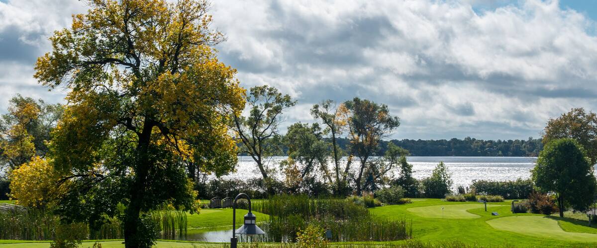 A golf course with a lake, trees, and a cloudy sky.