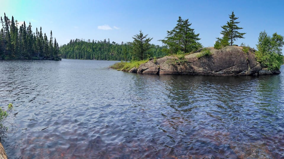 A calm lake surrounded by dense forest and rocky outcrops.