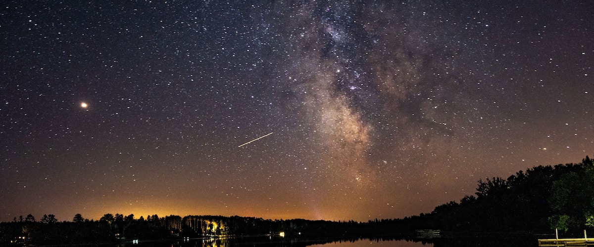 A starry night sky over a calm lake with the Milky Way visible.