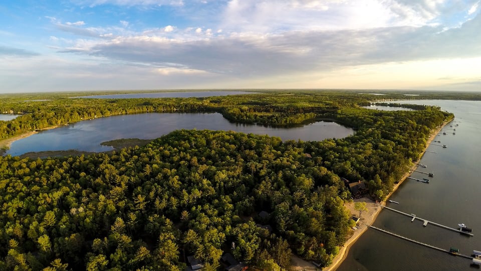 A large lake surrounded by dense forest, with several docks and boats along the shoreline.