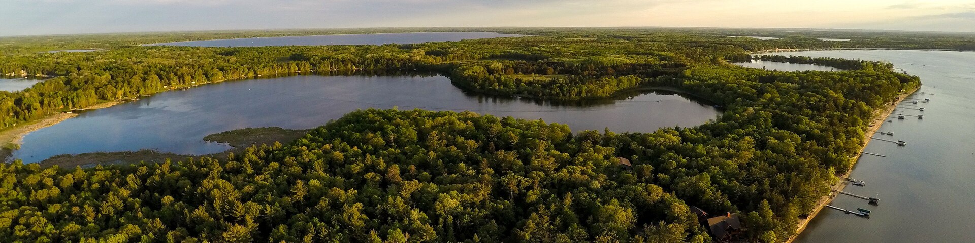 A large lake surrounded by dense forest, with several docks and boats along the shoreline.