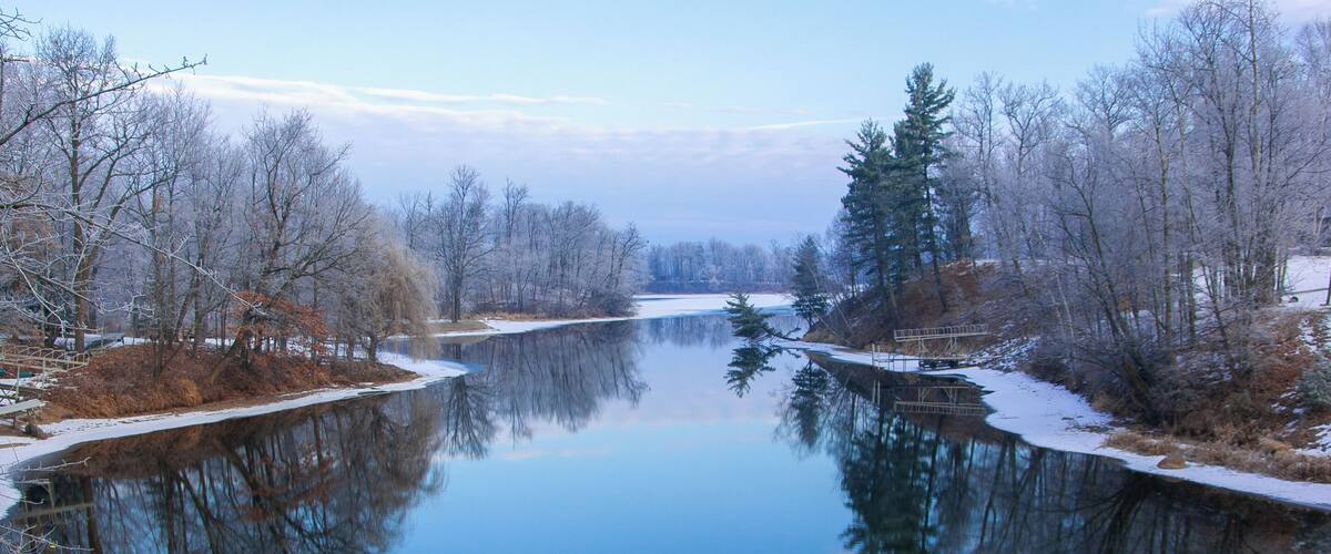 A calm river with reflections of trees and a wooden bridge.