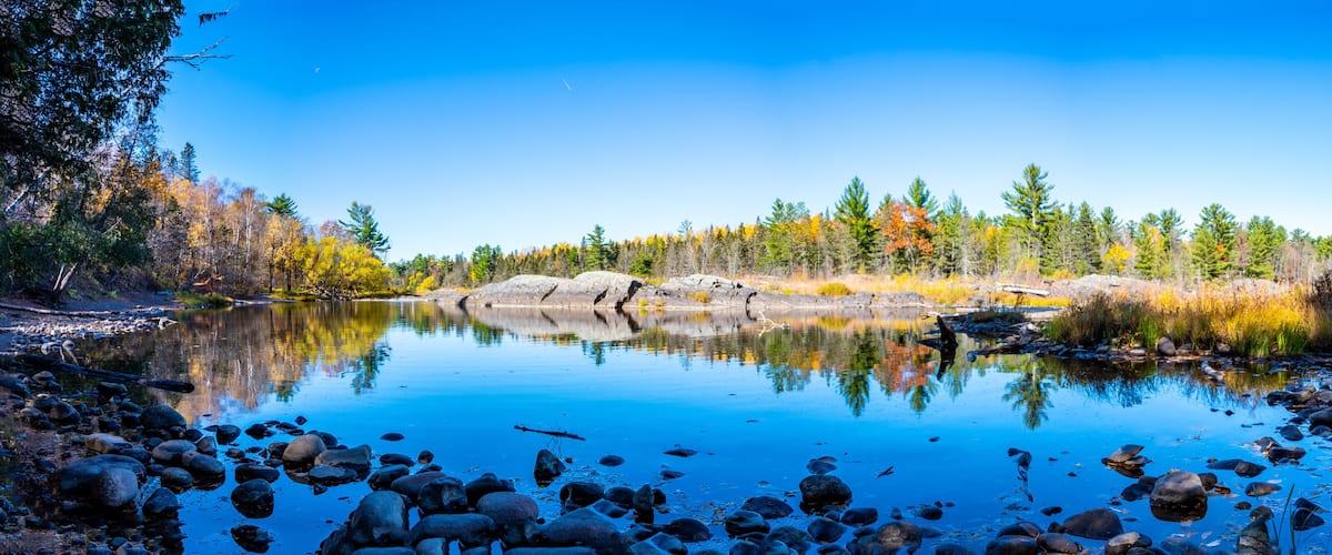 A calm lake surrounded by autumn-colored trees and rocks.