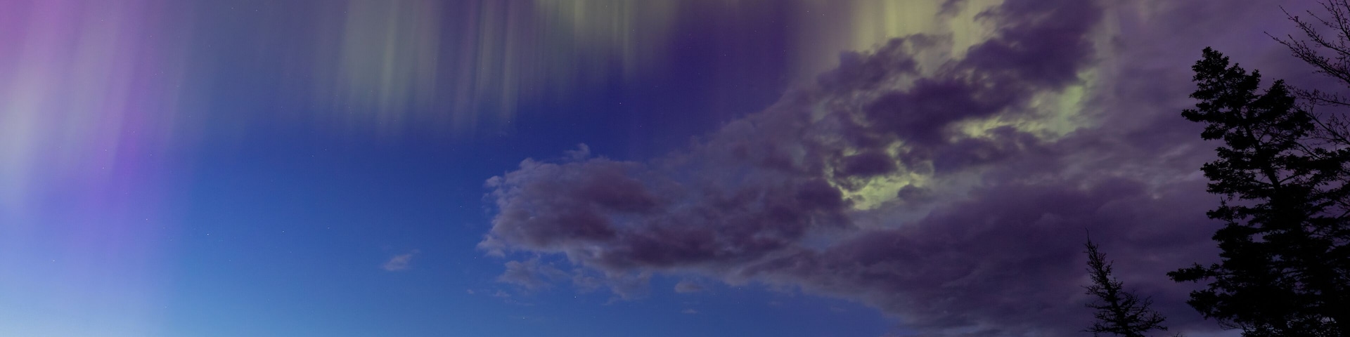 Northern lights erupt over a lake in Minnesota in a dark sky overhead shining rainbow of Aurora light as the sun sets on the horizon