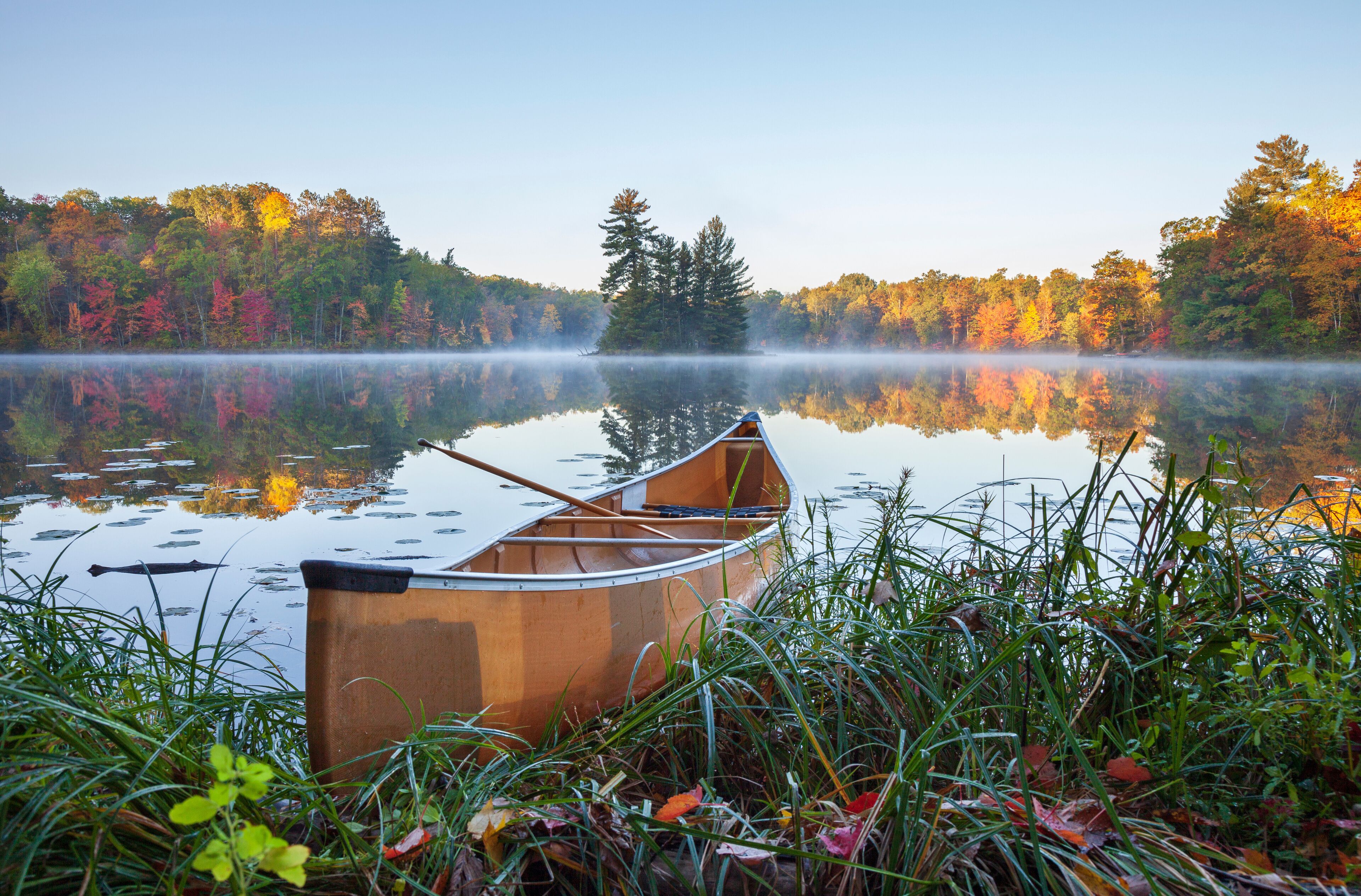 Yellow canoe on shore of calm lake with island and trees in fall color in northern Minnesota
