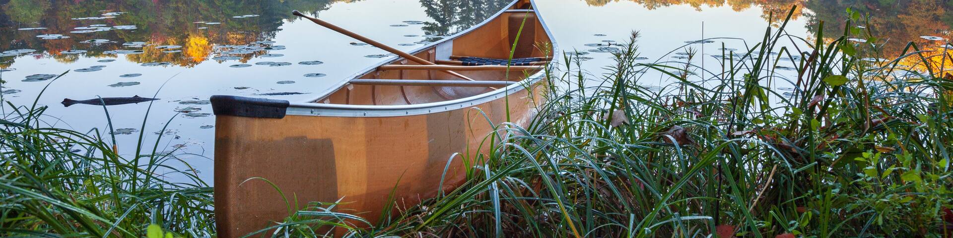 A wooden canoe on a calm lake with autumn foliage and a misty forest in the background.