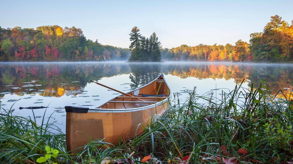 Yellow canoe on shore of calm lake with island and trees in fall color in northern Minnesota