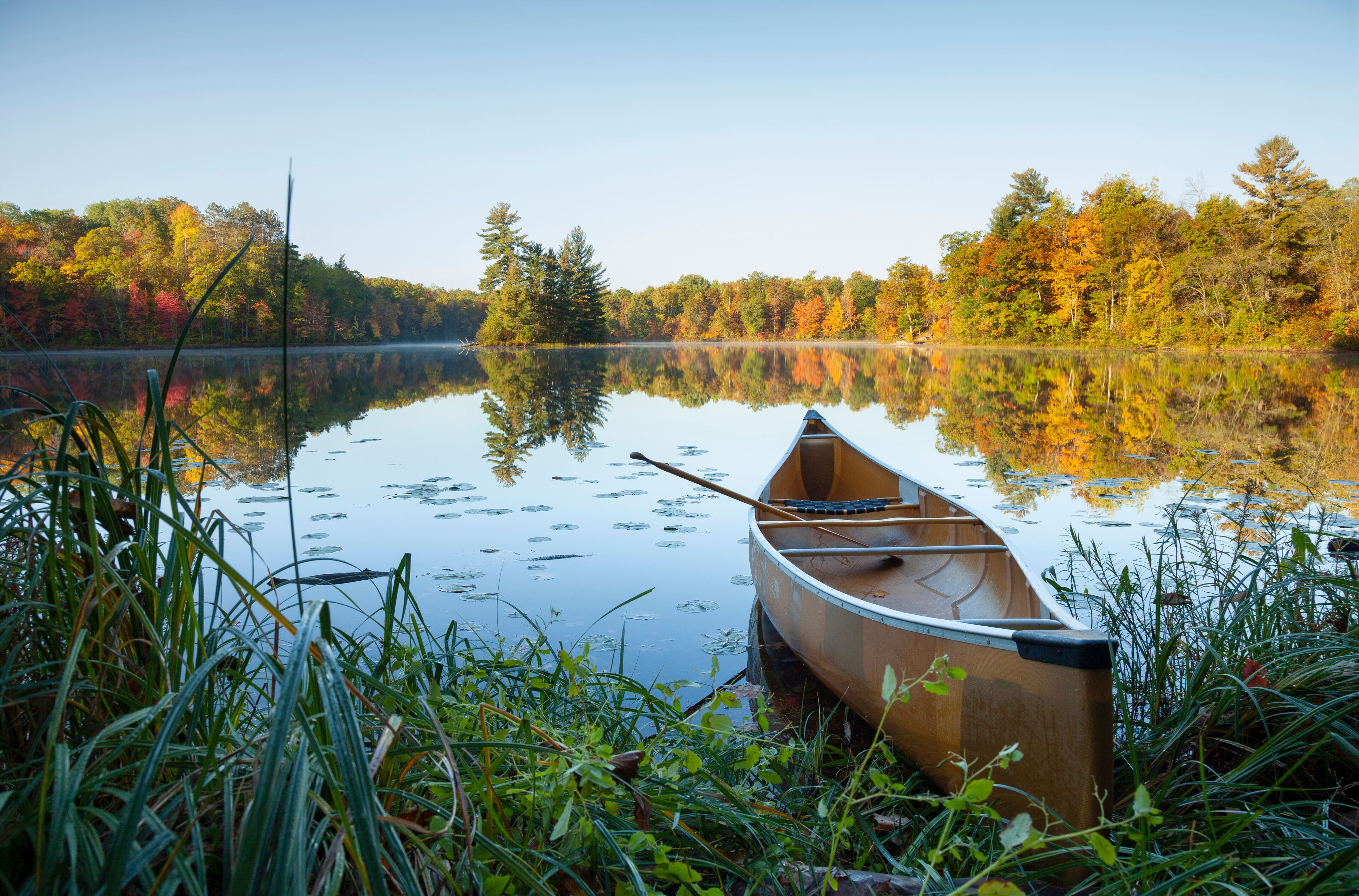 Canoe with paddle on shore of beautiful lake with island in northern Minnesota at dawn