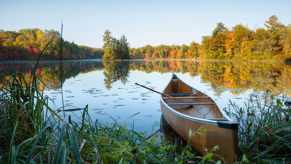 Canoe with paddle on shore of beautiful lake with island in northern Minnesota at dawn