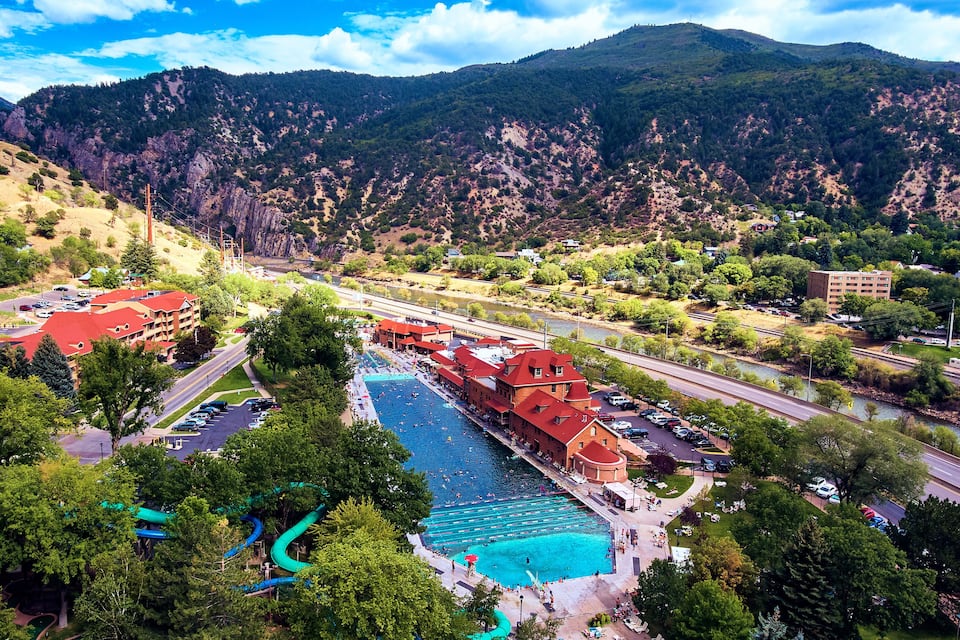 A resort with a swimming pool, red-roofed buildings, and a mountainous backdrop.