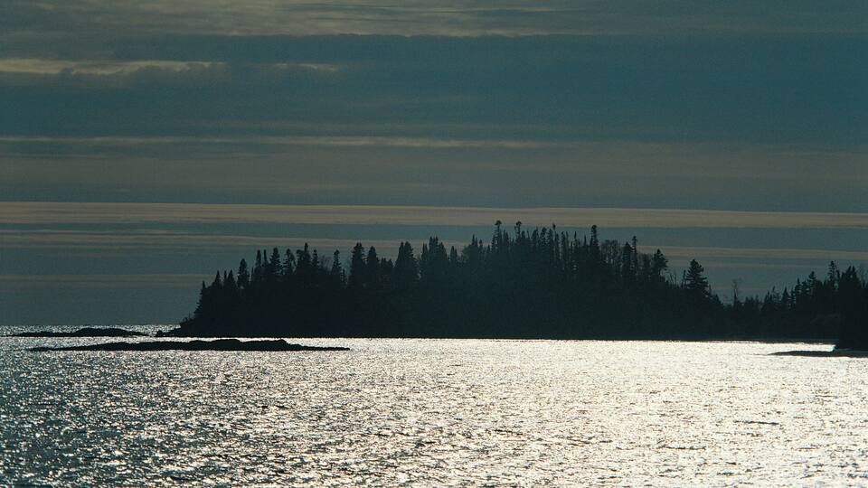 A calm sea with a forested island silhouette in the distance.