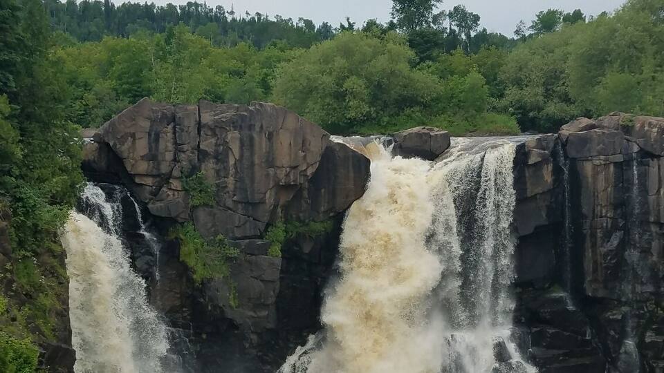 A powerful waterfall cascading over rocky cliffs surrounded by lush greenery.