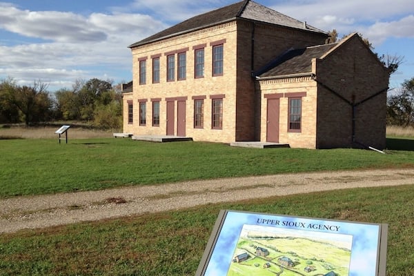 A historic Upper Sioux Agency building with a grassy field in front.