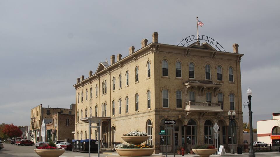 A historic building with a sign reading "NICOLLET" and a large planter in front.