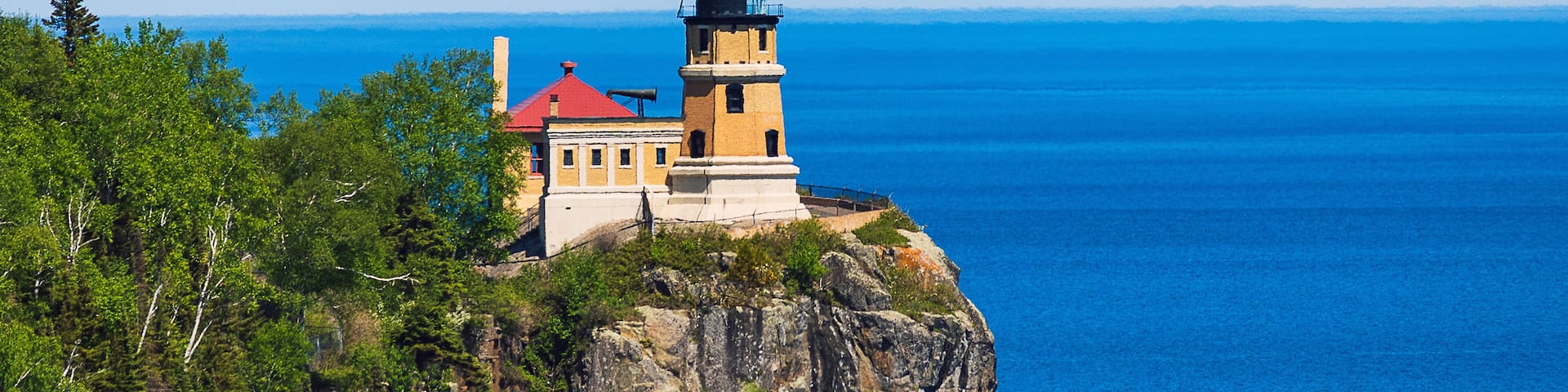 A lighthouse on a cliff overlooking a deep blue ocean.
