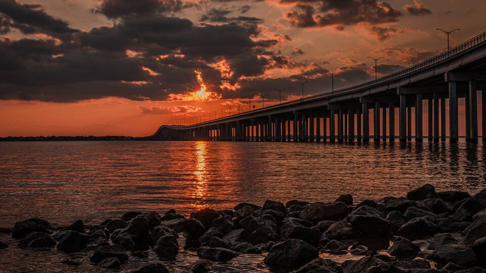 A sunset over a bridge with a rocky shoreline.