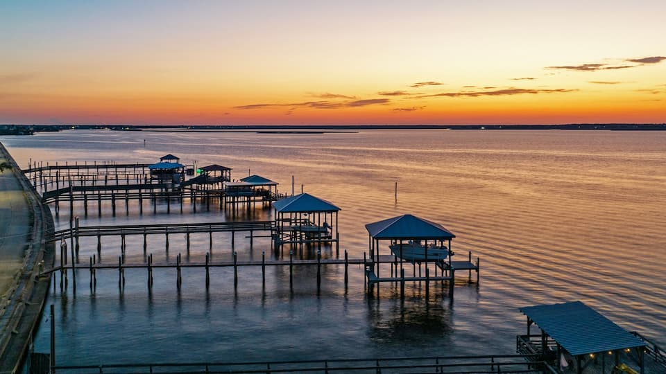 A waterfront with wooden docks and gazebos during sunset.