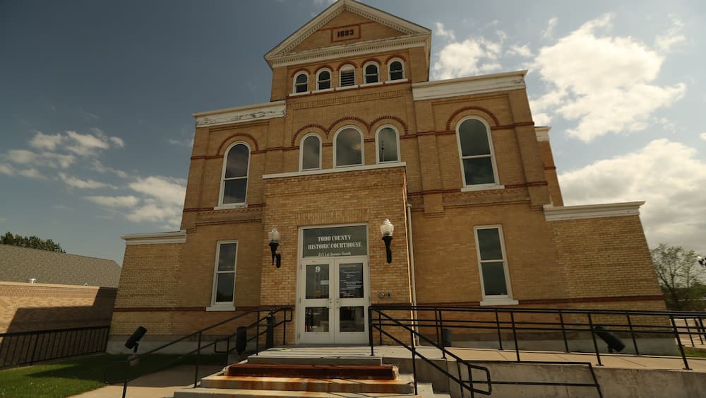 A historic courthouse with a prominent clock tower, arched windows, and a sign indicating its location.
