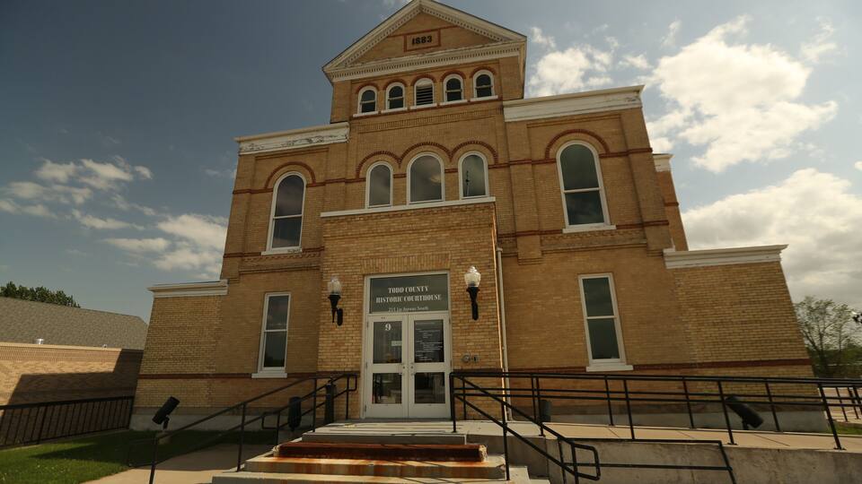 A historic courthouse with a prominent clock tower, arched windows, and a sign indicating its location.