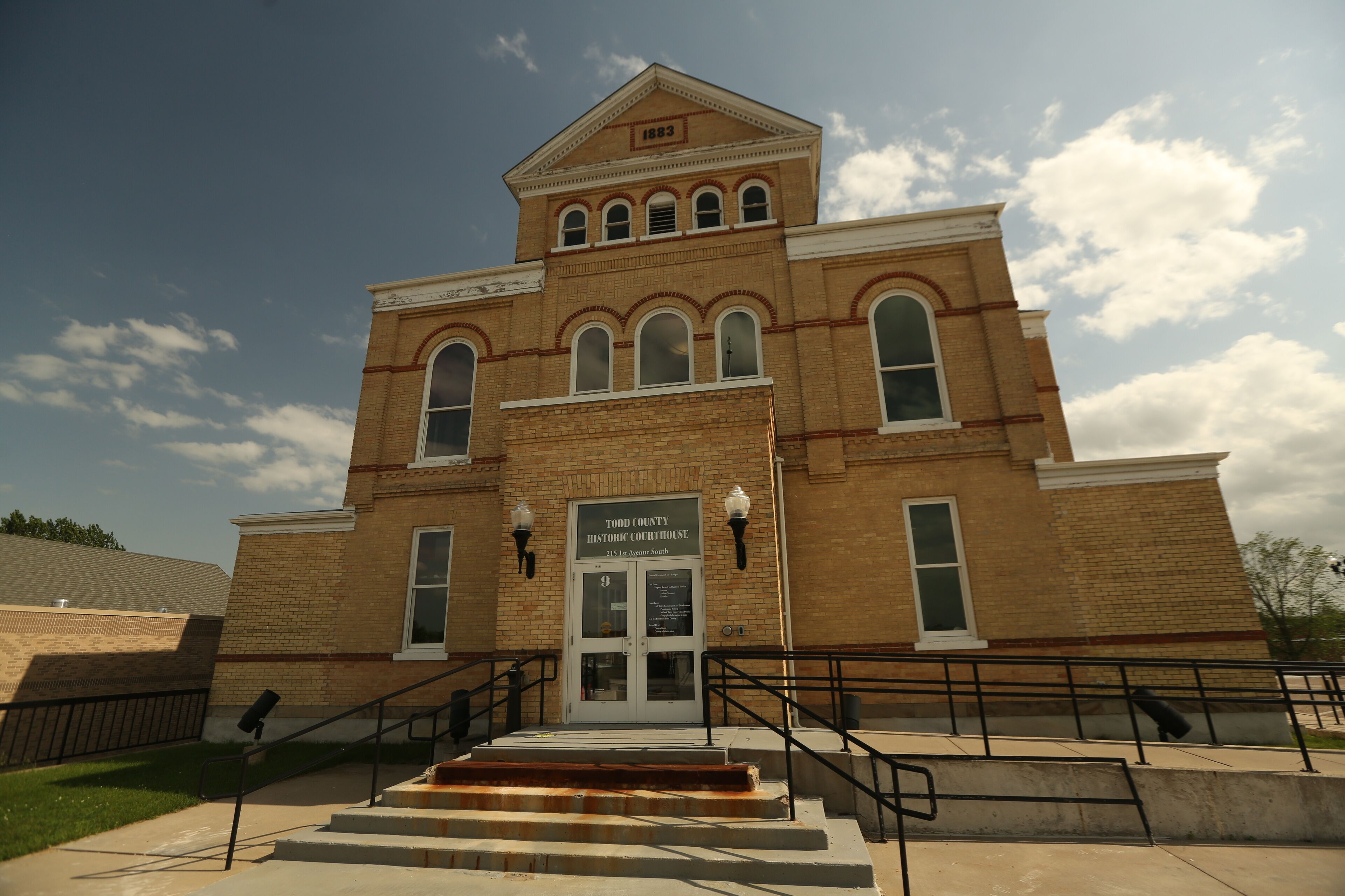 A historic courthouse with a prominent clock tower, arched windows, and a sign indicating its location.