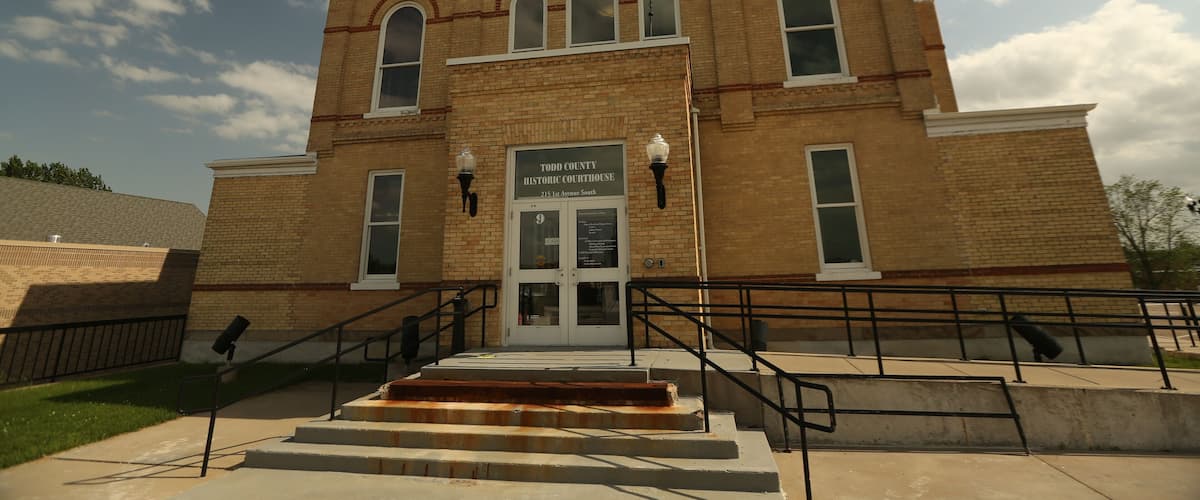 A historic courthouse with a prominent clock tower, arched windows, and a sign indicating its location.