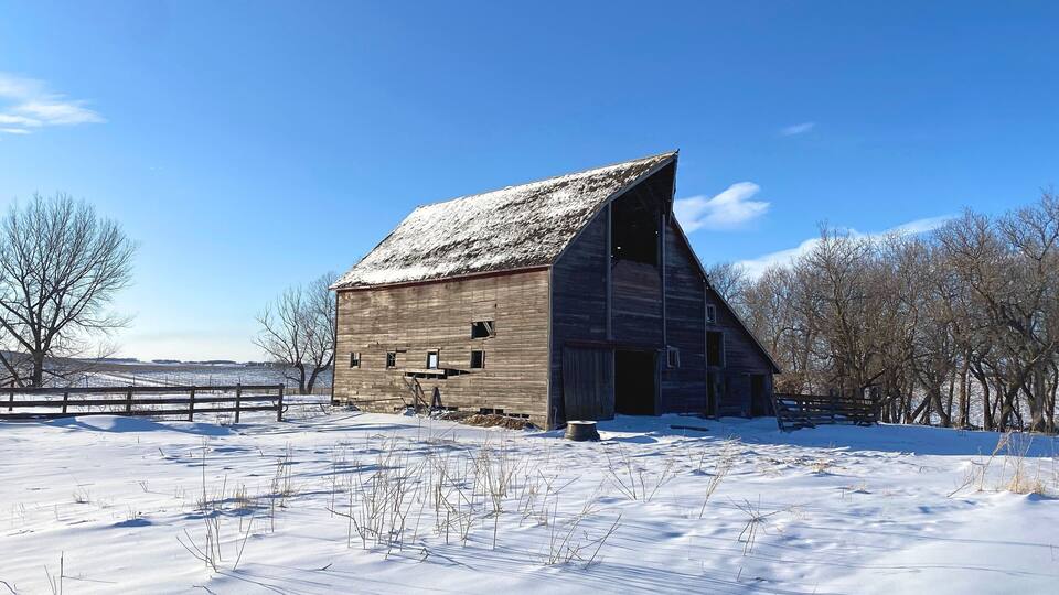 A snow-covered barn in a rural setting with a clear blue sky.