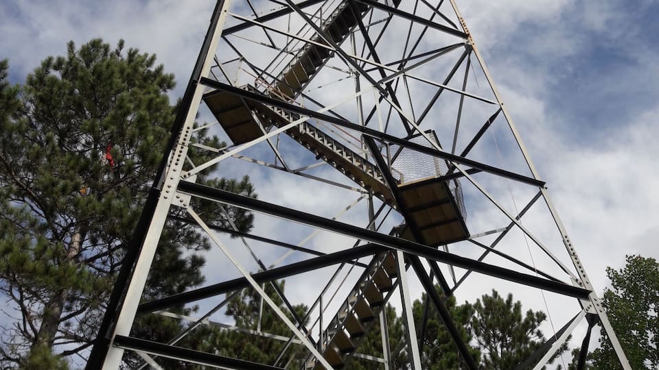 A tall metal structure with a staircase, surrounded by trees and a partly cloudy sky.
