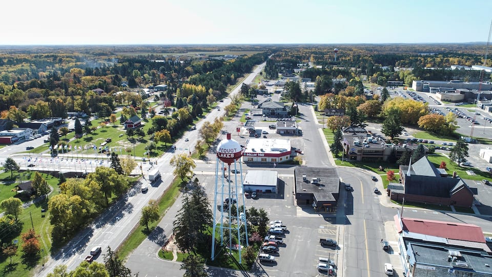 An aerial view of a town with a prominent water tower labeled 'Pequot Lakes,' a Dollar Tree store, and a mix of residential and commercial buildings.