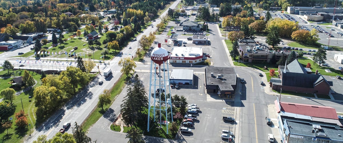 An aerial view of a town with a prominent water tower labeled 'Pequot Lakes,' a Dollar Tree store, and a mix of residential and commercial buildings.