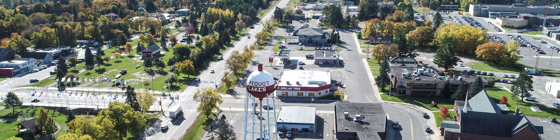 An aerial view of a town with a prominent water tower labeled 'Pequot Lakes,' a Dollar Tree store, and a mix of residential and commercial buildings.