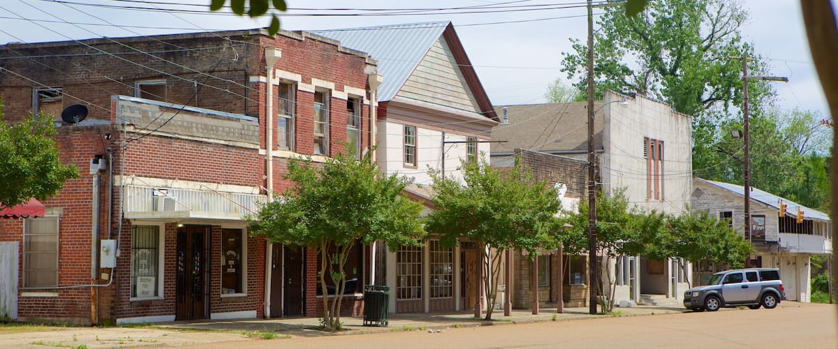 A street lined with historic buildings, including a red brick building with a 'Booths for Rent' sign and a white building with a sloped roof.