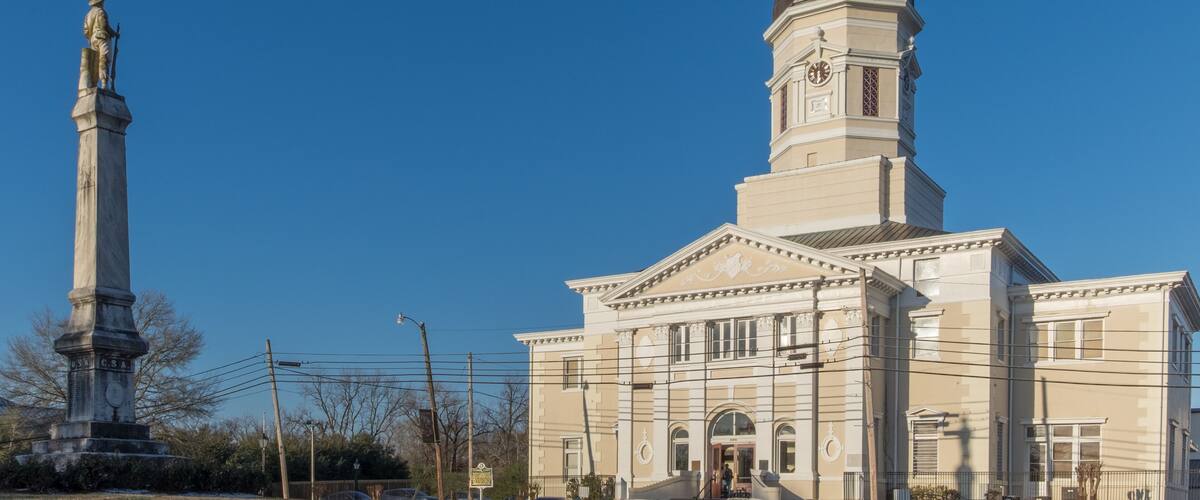 A large building with a clock tower and a statue in front.