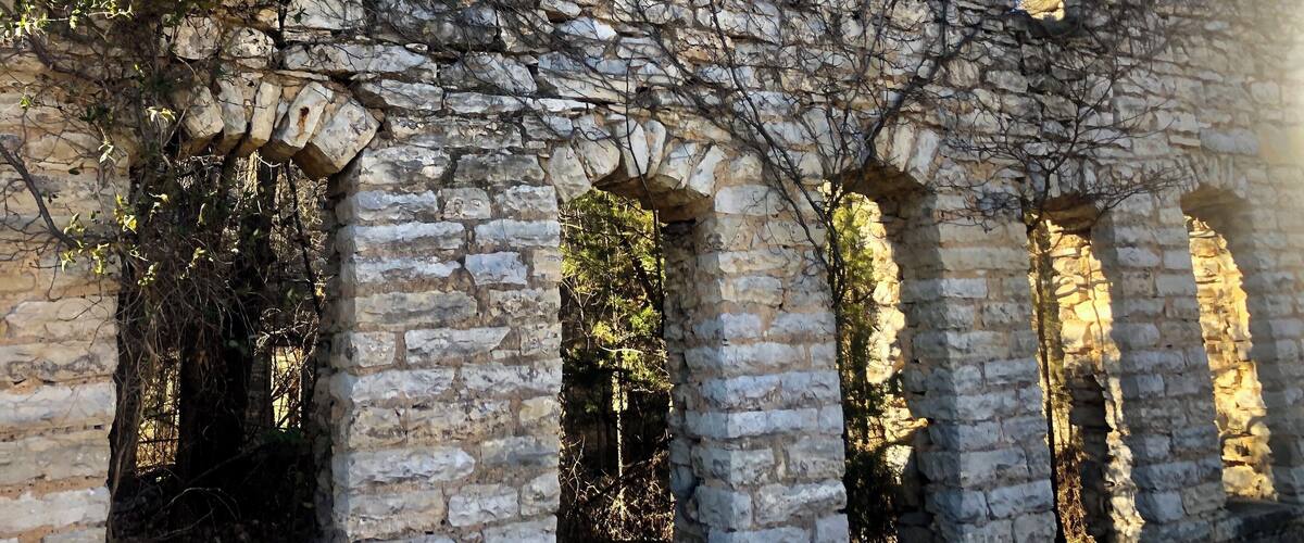 A stone building with arched windows and ivy growth.