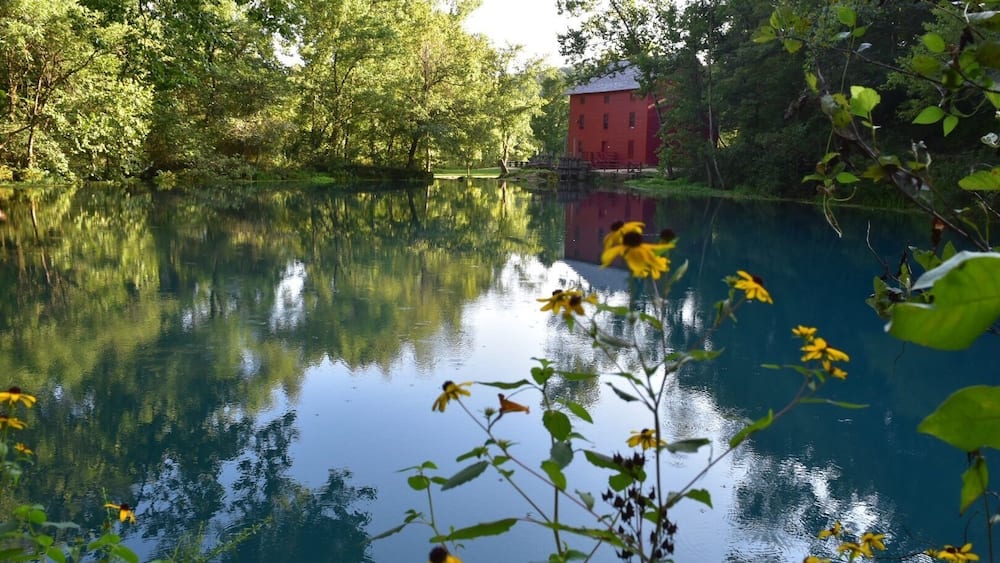 A calm lake with reflections of trees and a red building.