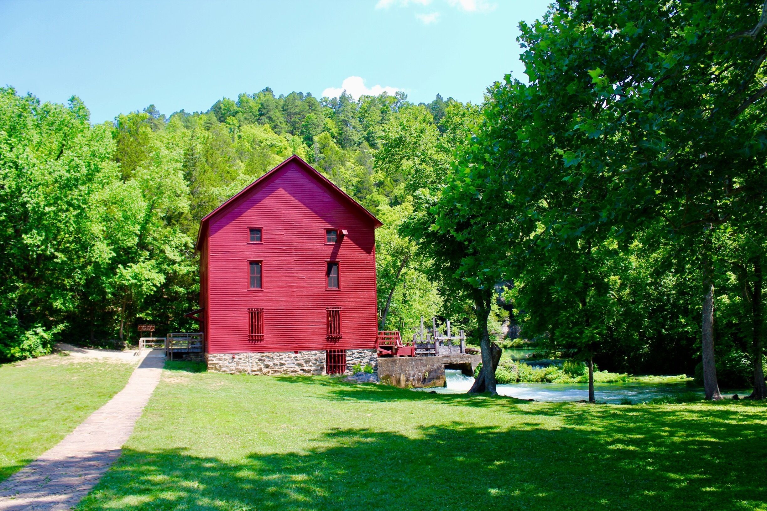 A red barn surrounded by lush green trees and a small stream.